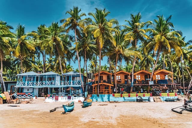 Beachfront huts and colorful shacks surrunded by tall palm trees on sunny in goa.best time to visit goa